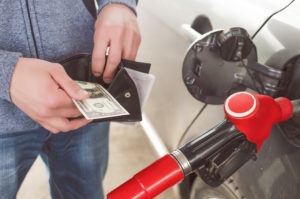 Person with open wallet and cash next to a gas pump