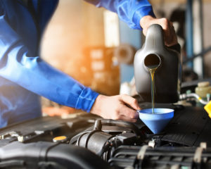 auto mechanic pouring motor oil into engine