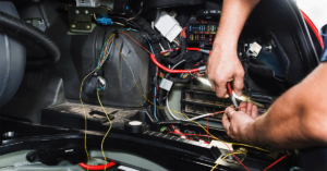 A mechanic tests electrical wires under the hood.