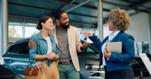 A car salesperson hands car keys to a couple who just purchased the automobile.