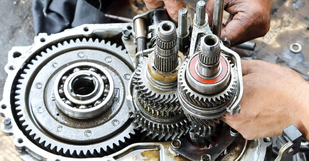 A pair of hands works on a car transmission.