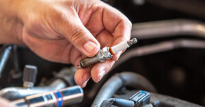 A well-manicured hand holding an automobile spark plug.