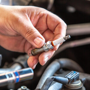 A well-manicured hand holding an automobile spark plug.
